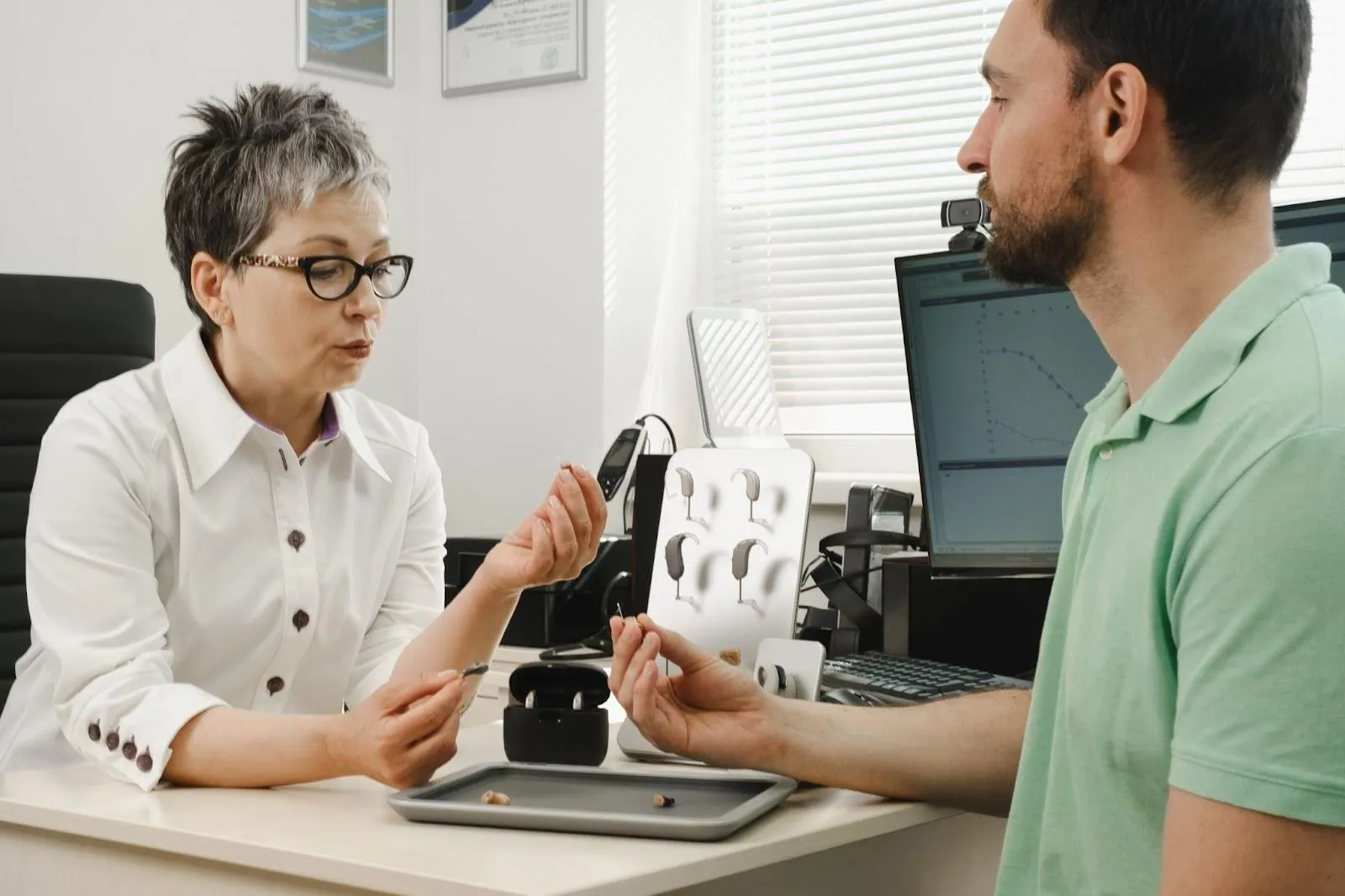 a_man_and_woman_sitting_at_a_desk_discussing_hearing_aids_audicus_mini
