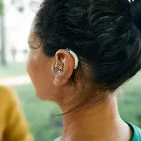 a_woman_in_a_green_dress_is_talking_to_another_woman_wearing_a_audicus_omni_2_hearing_aid