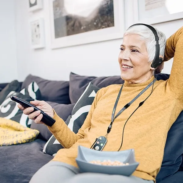 an_older_woman_sitting_on_a_couch_with_be_hear_smarto_headphones_on